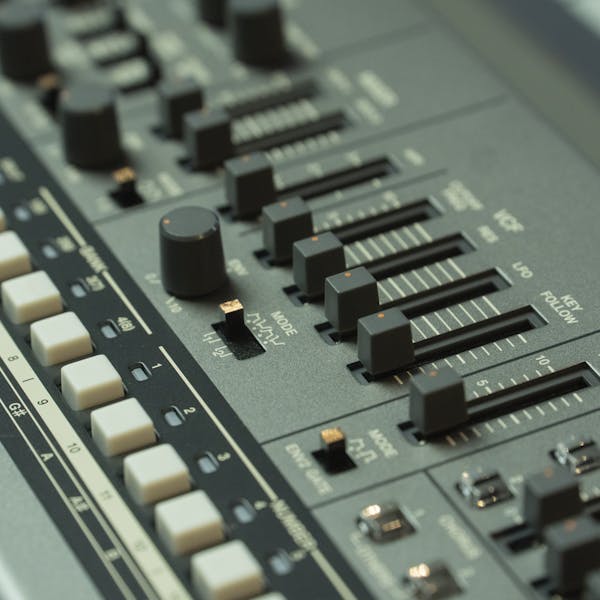 Detailed view of a music mixing console with various sliders and buttons in a studio setting.