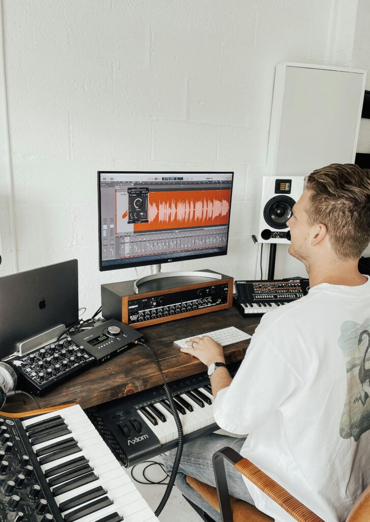 Music producer using digital audio workstation in a modern home studio.
