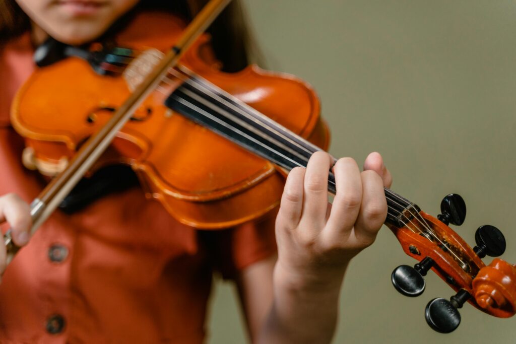 pexels-photo-8471819-8471819 Close-up image of a child playing the violin indoors, focusing on the strings and hand.